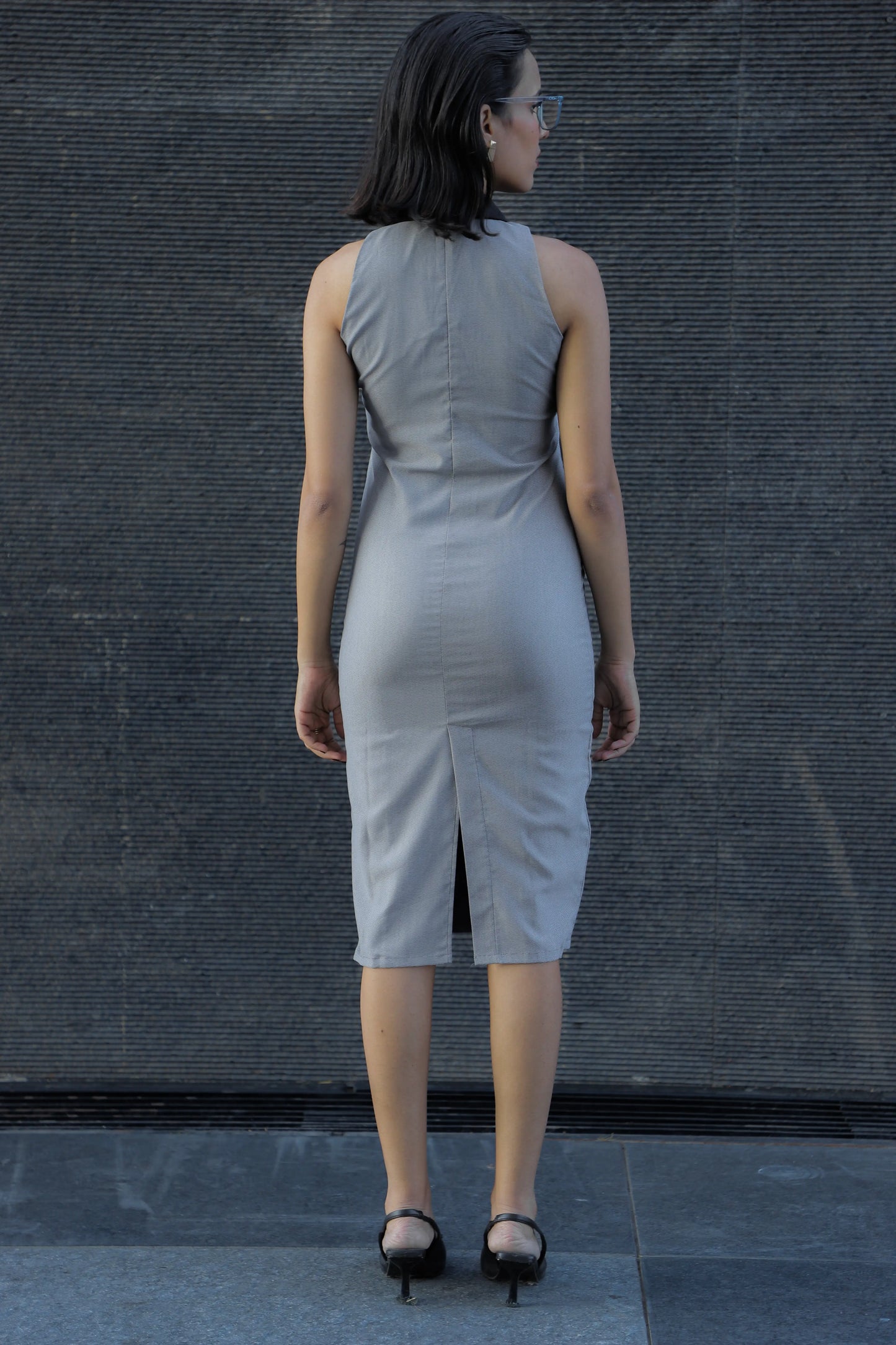 , MidWeek Women's Formal Wear - Workwear Style India, Woman wearing a light gray sleeveless dress against a dark textured wall.