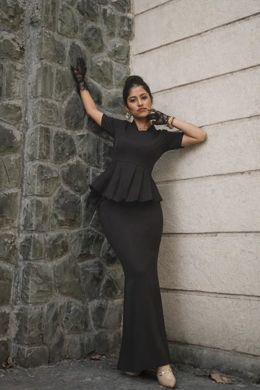Woman in a black peplum dress standing against a stone wall.