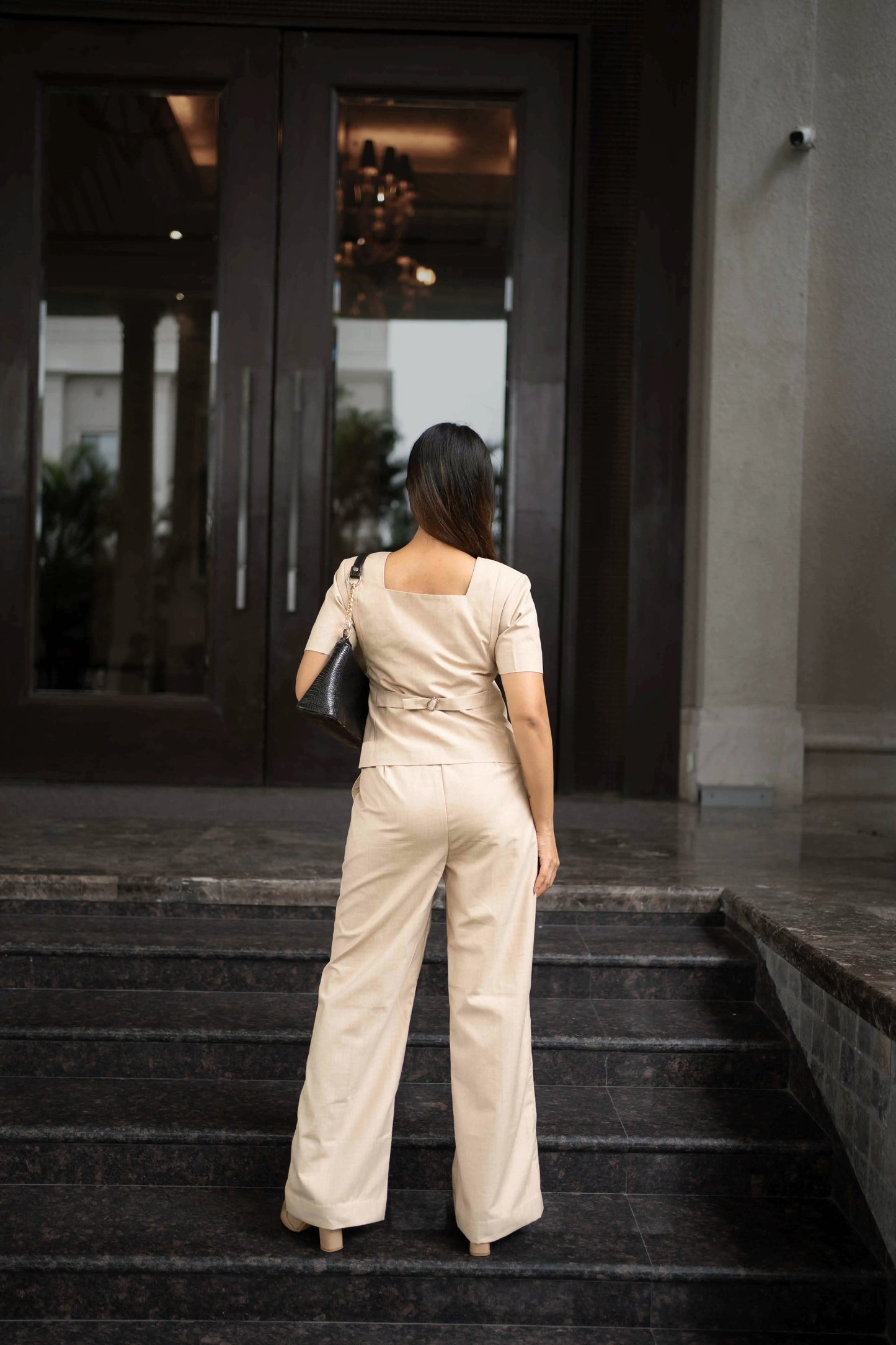 , MidWeek Women's Formal Wear - Workwear Style India, Woman in a beige jumpsuit standing on steps outside a building
