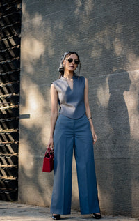 Woman in a blue outfit standing against a textured wall.