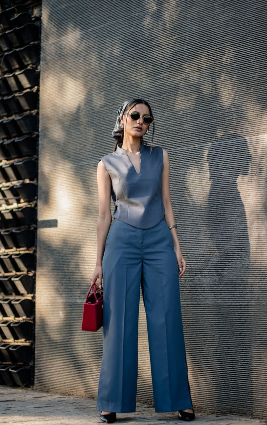 Woman in a blue outfit standing against a textured wall.