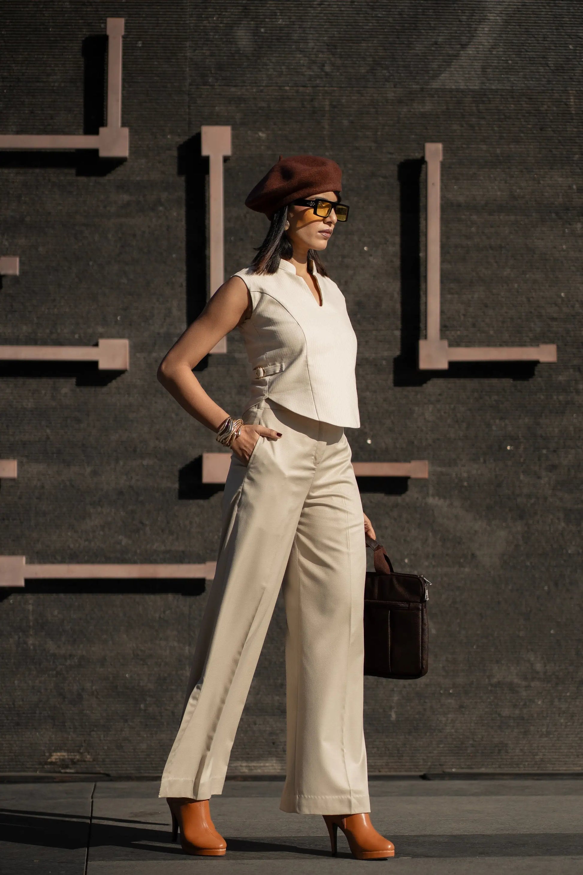 Woman in a white outfit with a red beret and sunglasses standing against a dark wall.