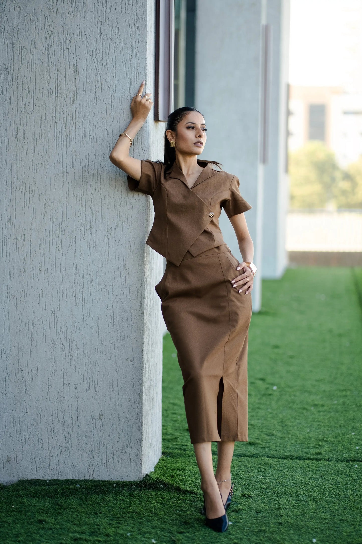, MidWeek Women's Formal Wear - Workwear Style India, Woman in a brown dress leaning against a wall on a grassy area.