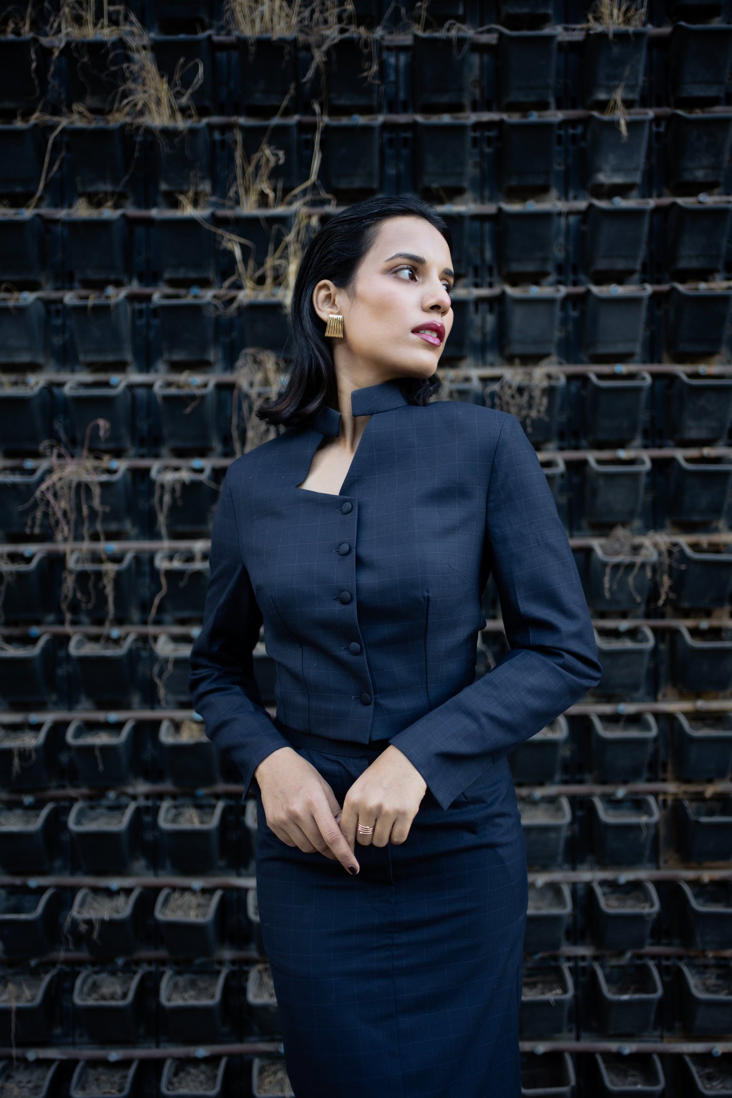 Woman in a navy blue outfit standing against a wall of black plant pots.