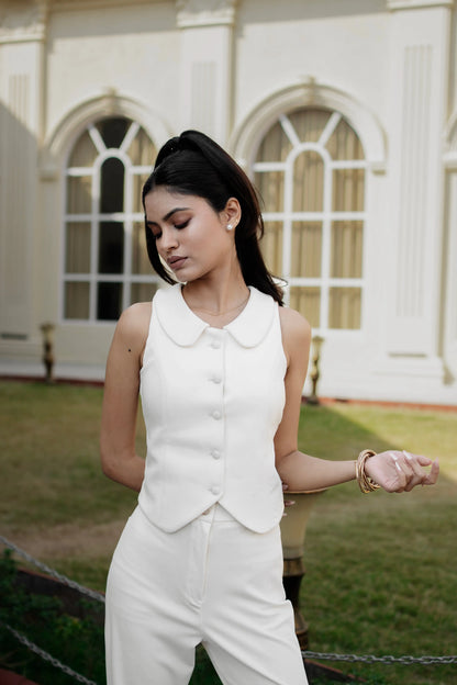 Woman in a white outfit standing in front of a building with arched windows.