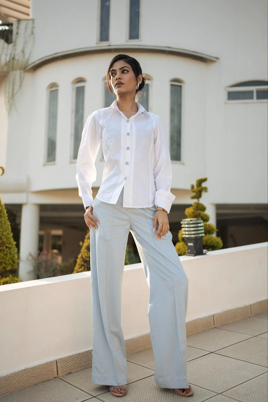 Woman wearing a white shirt and light blue pants standing on a rooftop with a building in the background.